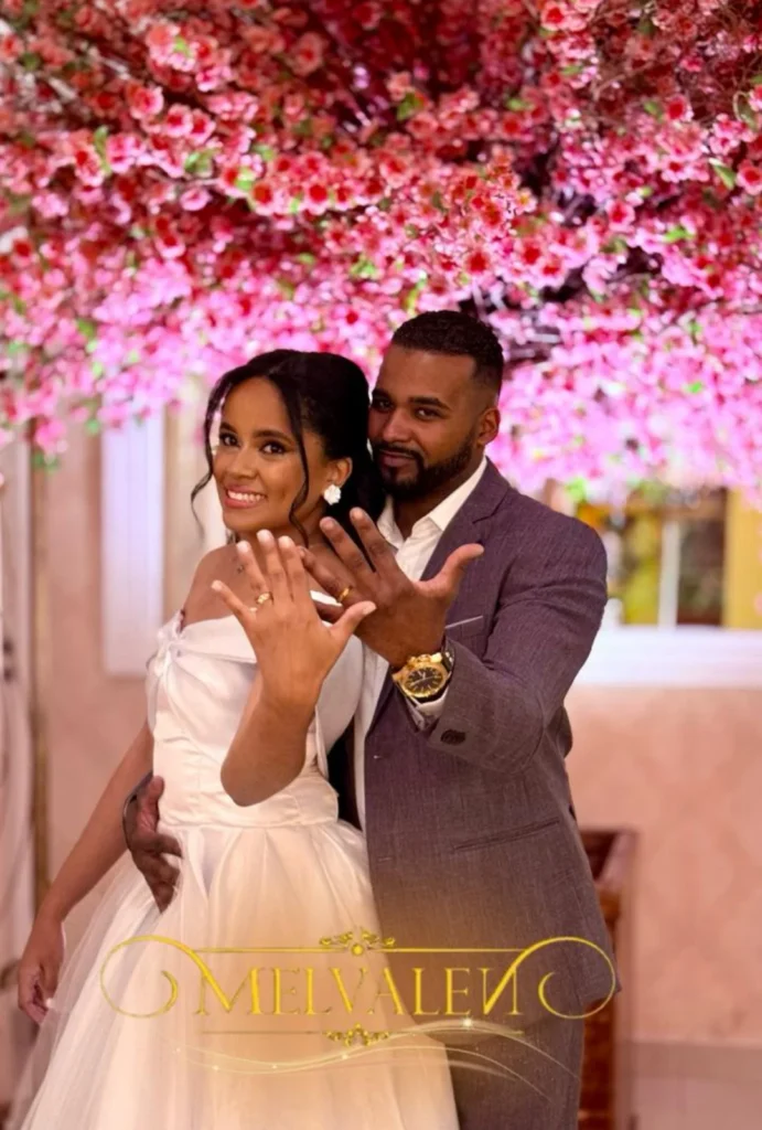 Casal de noivos mostrando as alianças sob um teto de flores cor de rosa no Buffet Melvalen