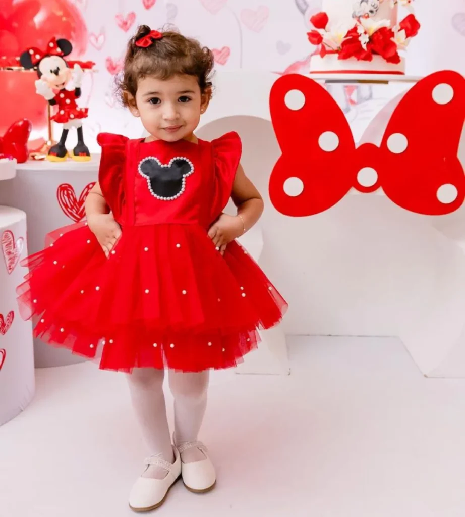 Menina de vestido vermelho em festa infantil com tema da Minnie, com laço vermelho ao fundo